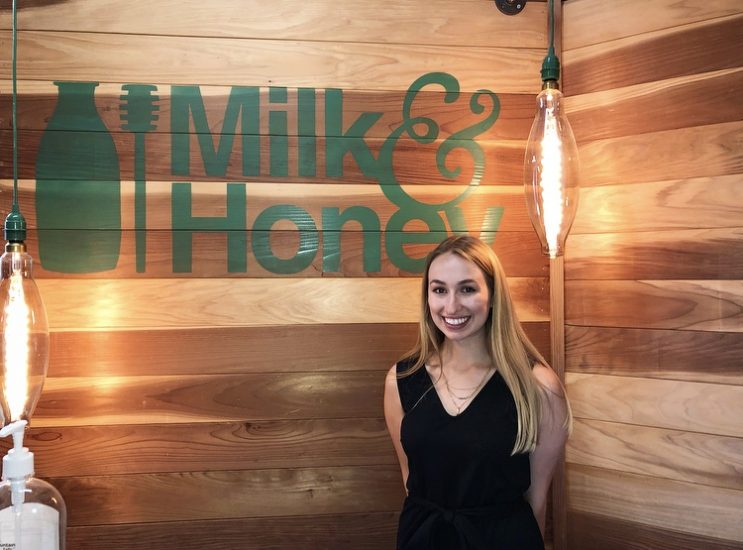 Ashleigh stands in front of Milk & Honey logo
